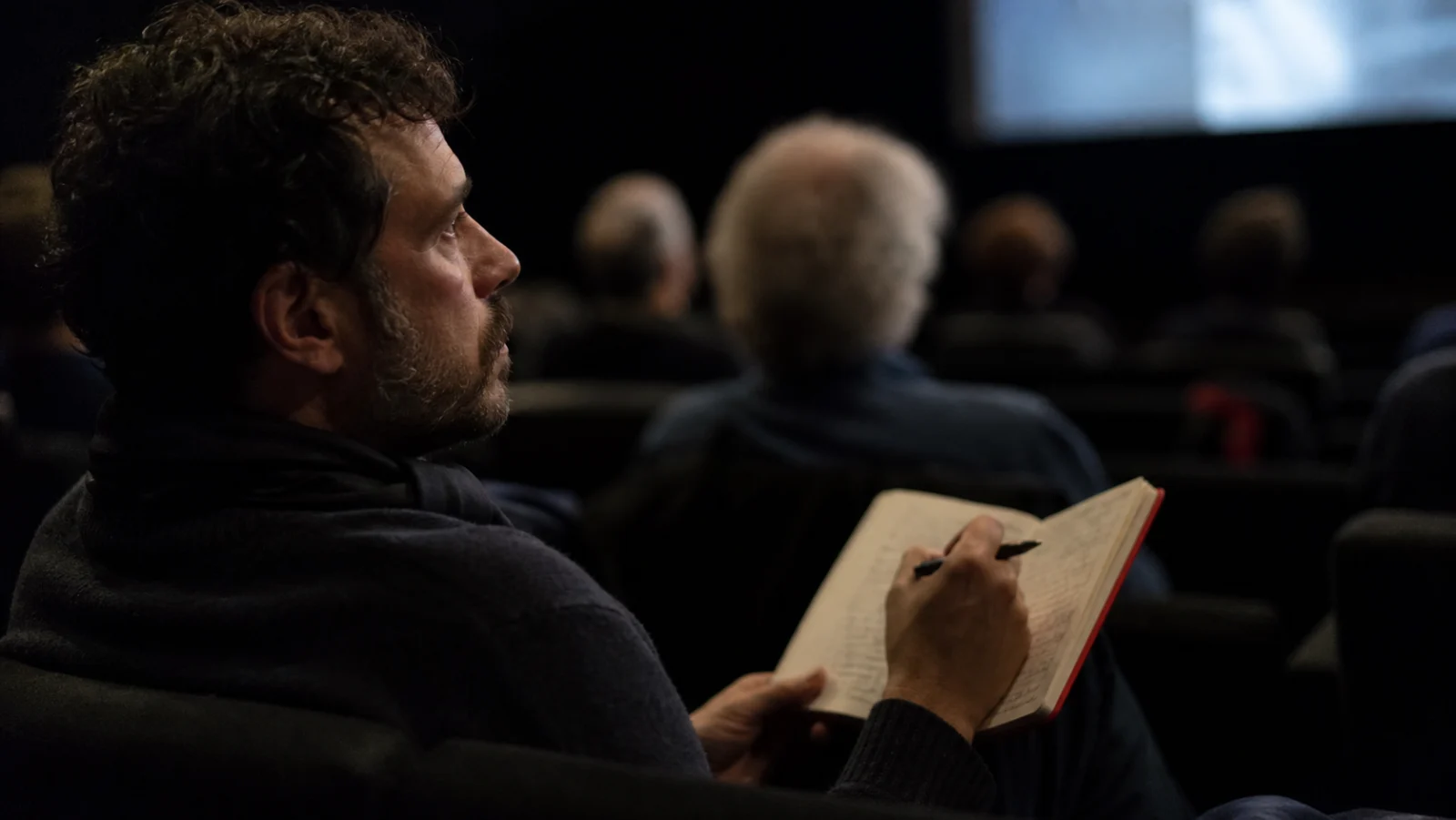 Viewer taking handwritten notes during an independent documentary screening