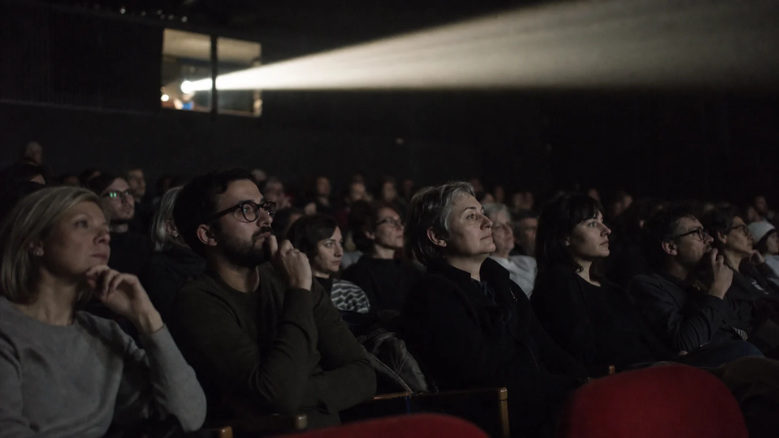 Film projector beam crossing a dark auditorium with viewers watching closely